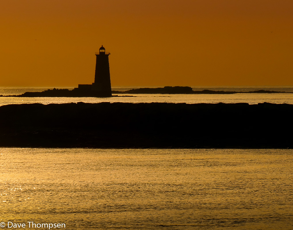 A silhouette photograph of Whaleback Lighthouse at sunrise in Portsmouth Harbor, New Hampshire.