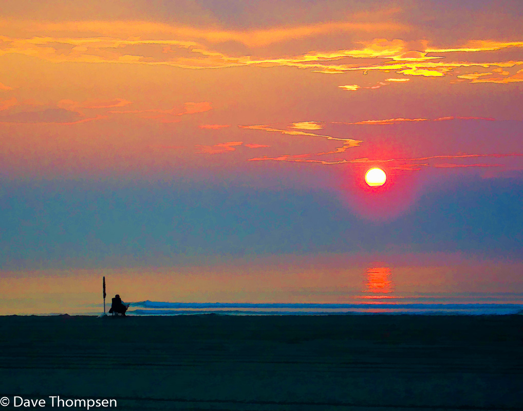 A photograph of a solitary soul, umbrella at the ready, sitting on Hampton Beach (NH) as the sun rises on a summer day.